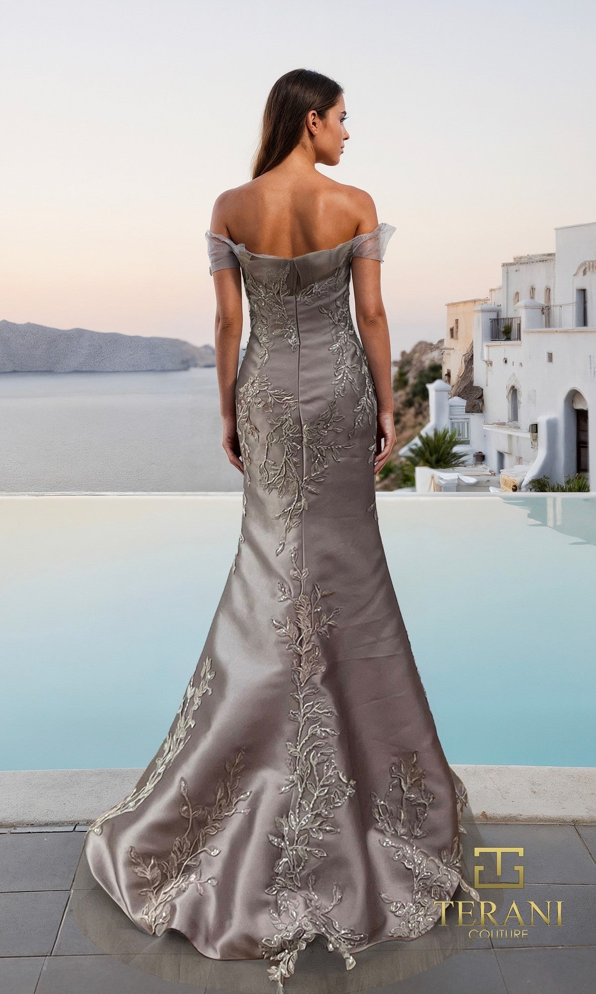A woman in the Terani 261E6270 long formal dress stands by a pool overlooking the sea and white Mediterranean-style buildings at sunset.
